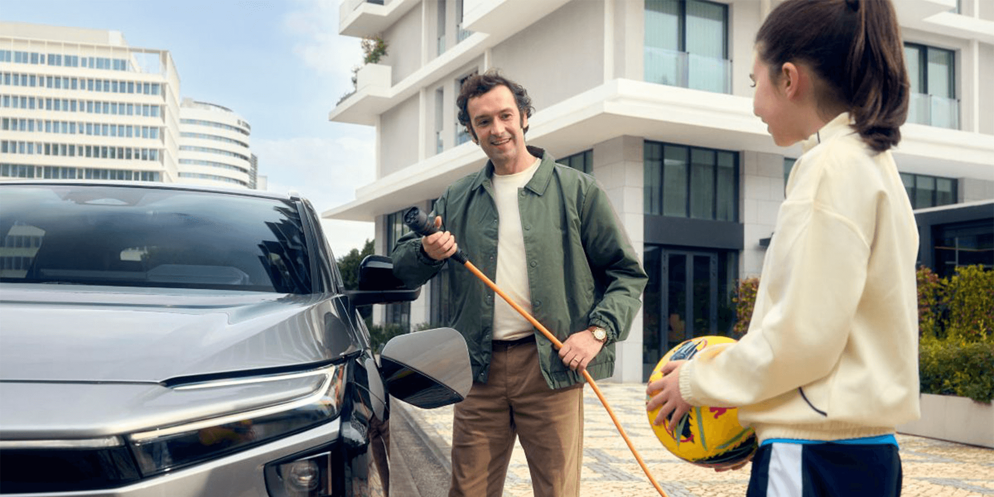 Eine Frau mit einem Ball in der Hand und ein Mann mit einem Stecker neben einem Auto.